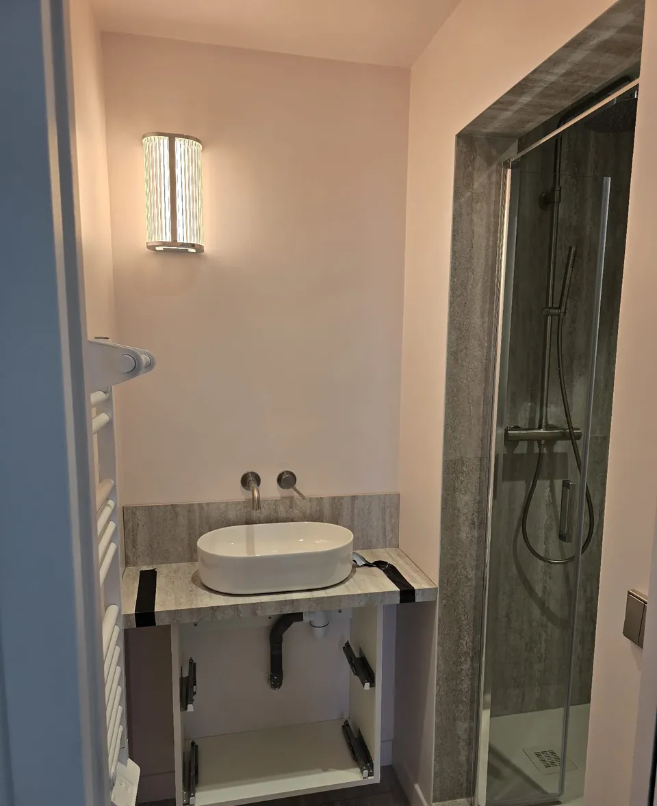 Salle d'eau avec vasque posée sur plan en pierre et cabine de douche vitrée